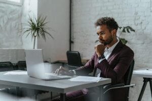 Un homme d'affaires en tenue d'entreprise se concentre sur le travail sur ordinateur portable dans un environnement de bureau moderne.